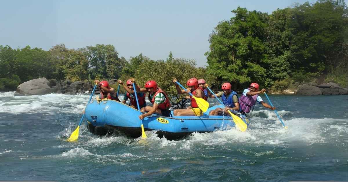 A group of people wearing helmets and life jackets rafting through whitewater rapids in a blue inflatable boat.